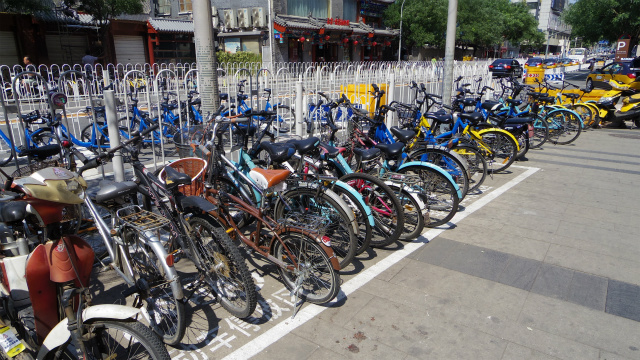 色んな色のシェアサイクルと個人の持ち物の自転車、スクーターがバラバラに並んでいる